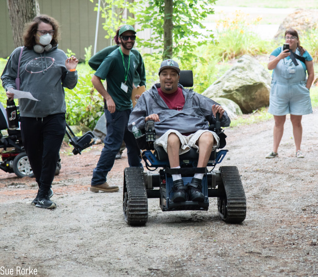 Man in all terrain chair with friend as staff looks on